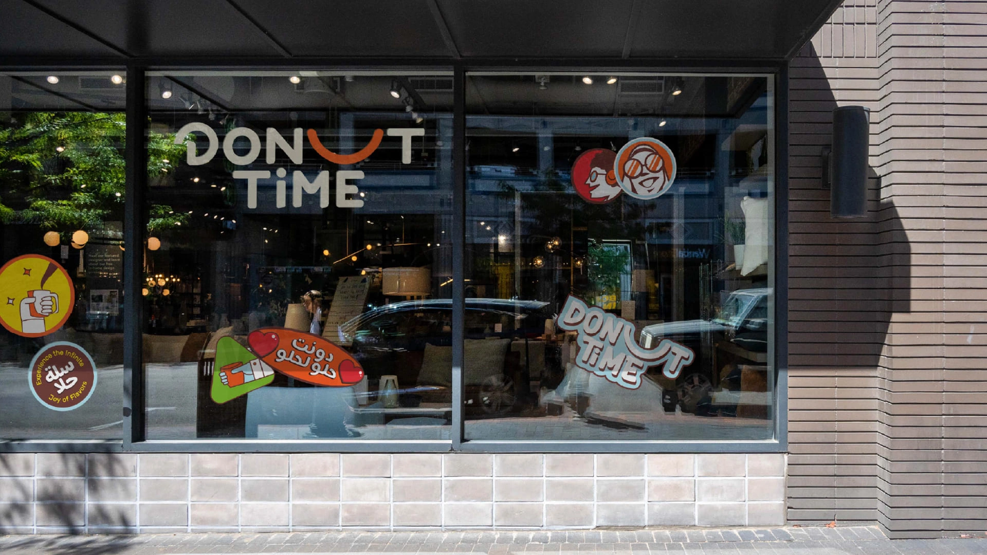 Donut Time rebrand: sky-blue carrier box with the orange smile logo and the Arabic line مكان لكل العيلة, held up against the sky