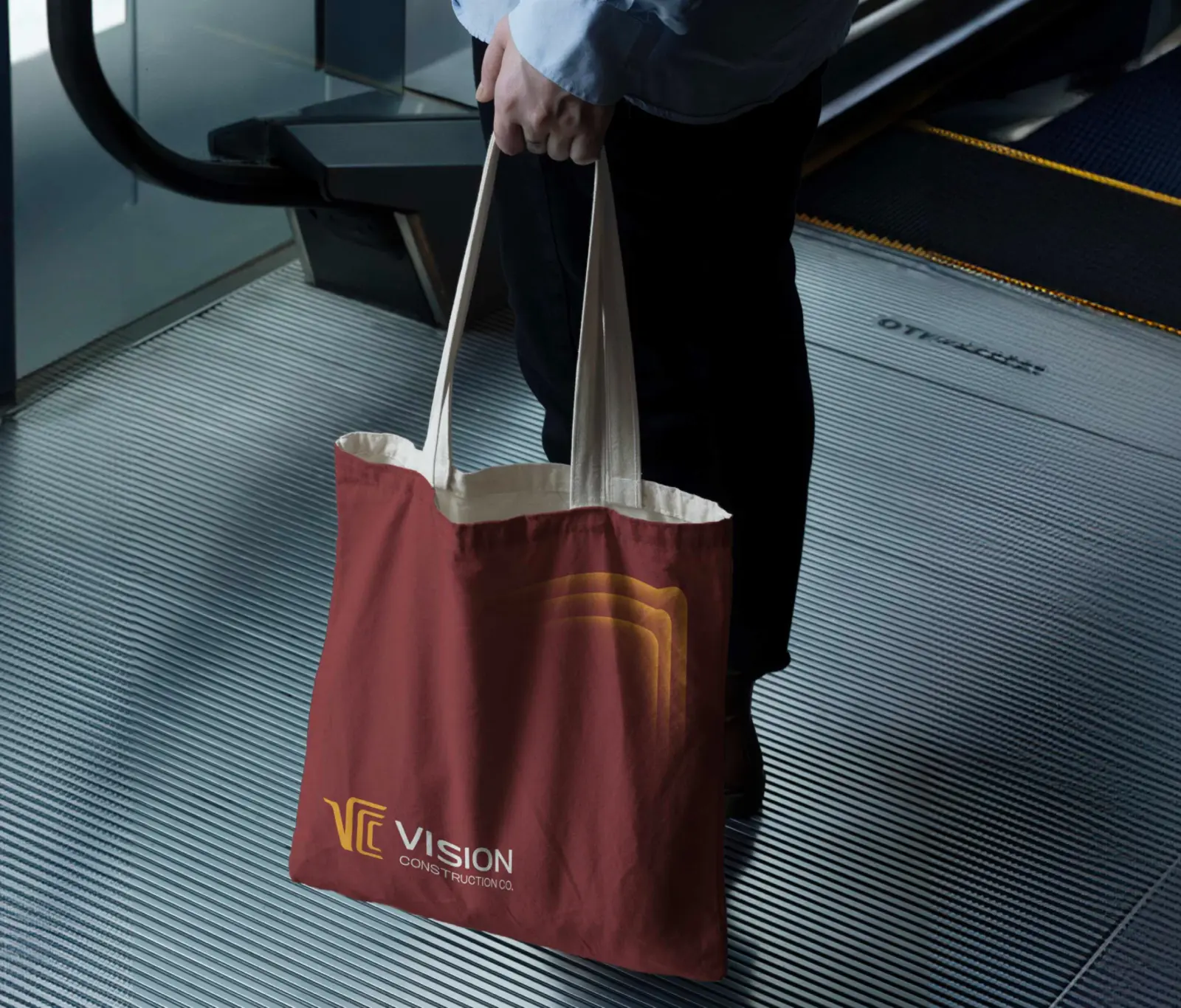 Person carrying a dark red VCC tote bag with the golden ripple graphic on an escalator