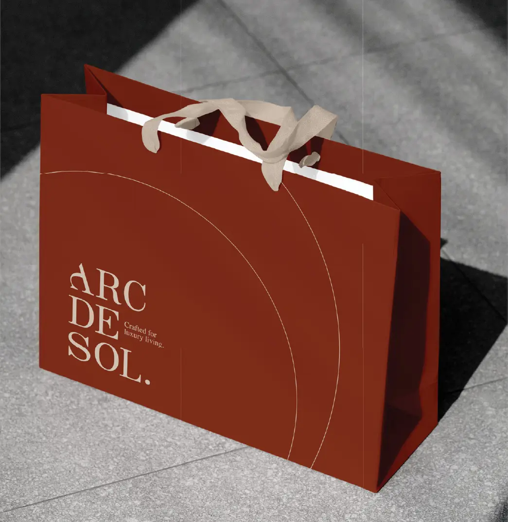 Warm red Arc de Sol shopping bag with cream rope handles and the stacked serif logo
