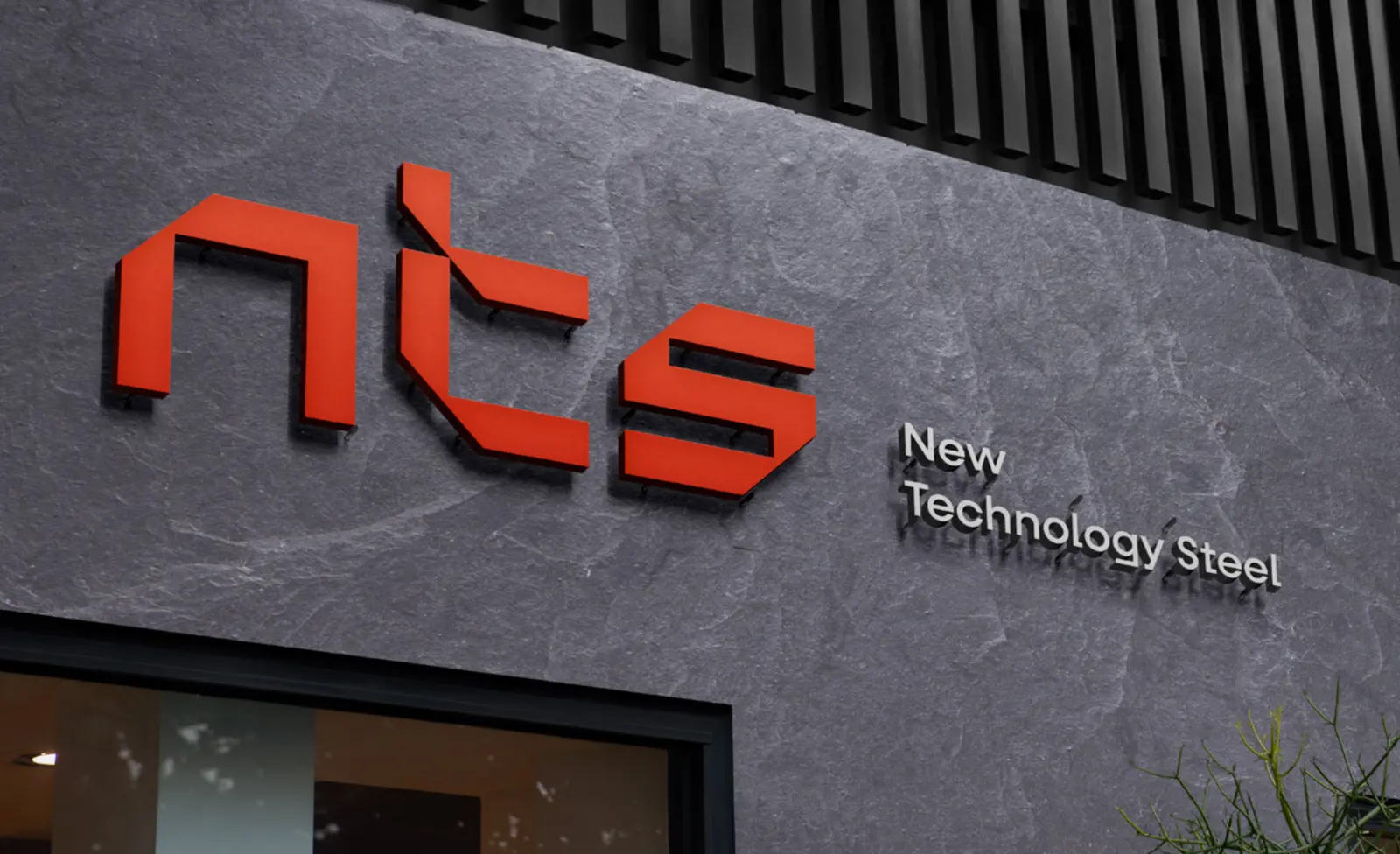 NTS facade sign with large orange 3D letters and New Technology Steel in brushed steel on a dark stone wall