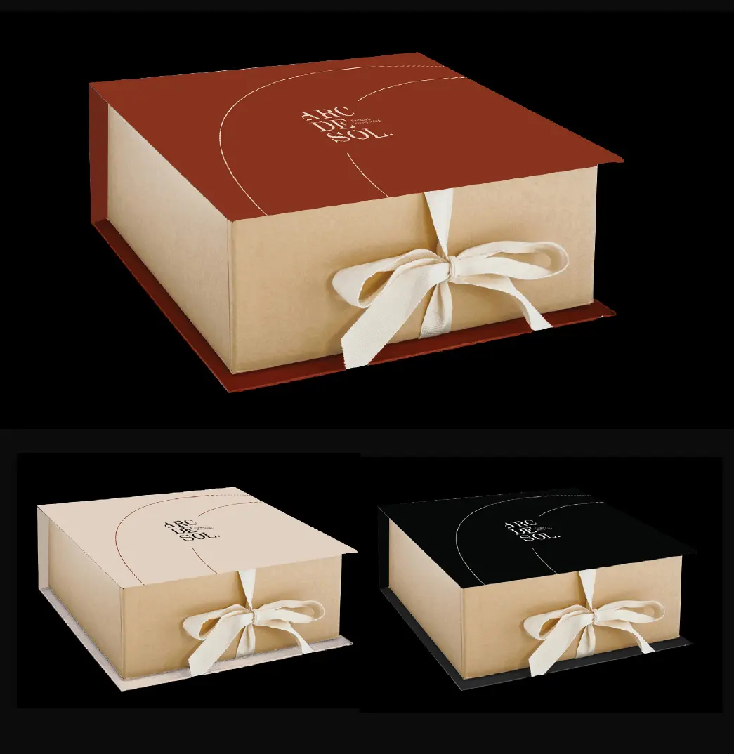 Three Arc de Sol gift boxes in warm red, stone and black, each tied with a cream ribbon